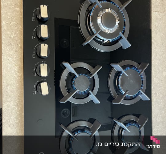 כיריים גז עם ארבעה מבערים דולקים על משטח מטבח.